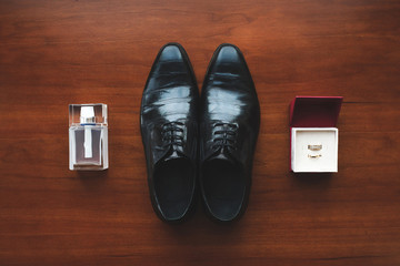 Black shoes, engagement rings and men's perfume on the floor. Ac