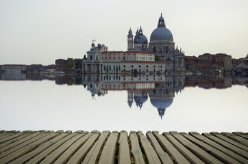 Fototapeta premium Fine art image with Grand Canal and Basilica Santa Maria della Salute, reflected on the water surface, with wood planks floor for foreground, Venice, Italy.