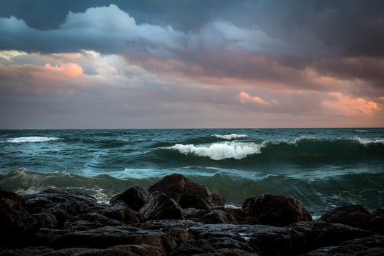 Fototapeta l'écume des vagues d'une mer verte sous le ciel orageux, et près de rochers noirs