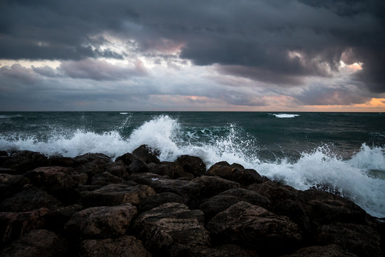 Fototapeta l'écume des vagues se fracassant sur les rochers noirs sous un ciel sombre 