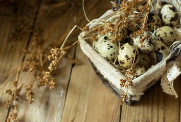 Quail eggs in a lined wire basket, on straw, with beige dry flowers on barn wood background, Easter, rustic vintage style, kinfolk, simplicity, top view, close up