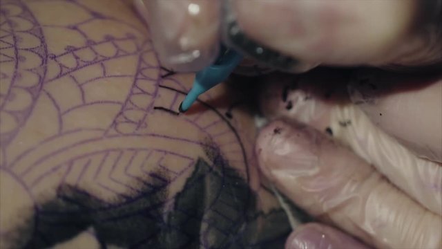 Close-up of hands of tattoo artist in gloves tattooing a pattern on body macro HD