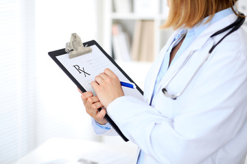 Close up of  female doctor  writing a medical prescription at clipboard while standing