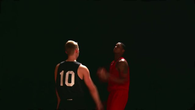 A basketball player defends an opponent, against a black backdrop