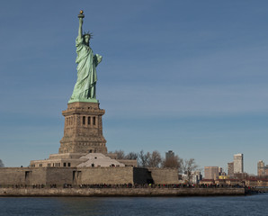 Obraz premium View of Liberty Island and the Statue of Liberty with unrecognizable tourist crowd on the bottom, skyscrapers in the background and the ocean water in the foreground
