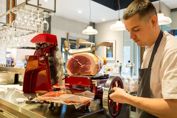 young European Italian chef slicing cutting parma ham cure meat Iberia on red collar slicer...