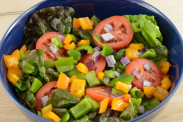 Closeup of Salad in blue bowl with red leaf lettuce, sliced tomatoes and chopped green onions, green and orange chopped bell peppers