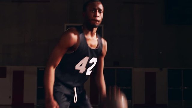 Close up on a basketball player on the court dribbling toward the camera, dark lighting