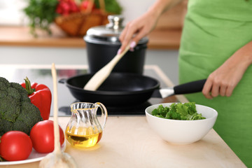 Fresh vegetables, salad and vegetable oil at the background of  woman is cooking by the stove in the kitchen