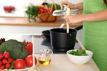 Young woman is cooking by the stove in the kitchen, close up.