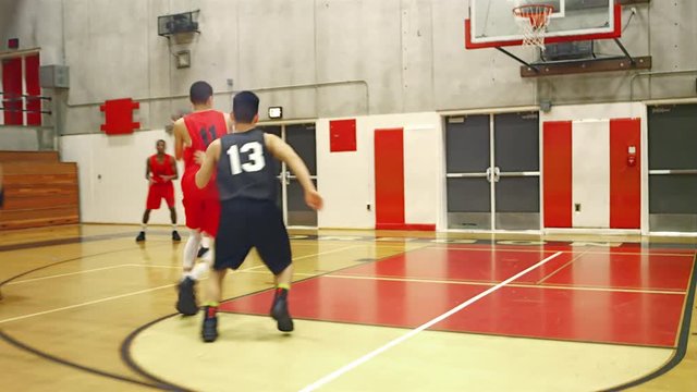Basketball players passing the ball down the court during a game and making a slam dunk