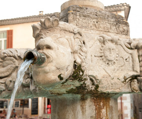 Fototapeta na wymiar Stone carved water faucet pouring water at town center well in France. 