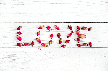 Word Love with rose buds on a white wooden background