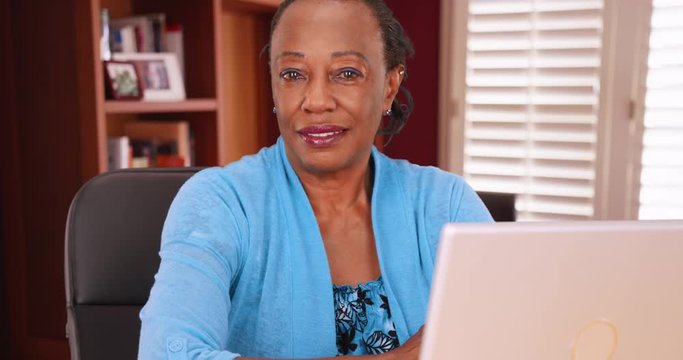 An African American businesswoman poses for a portrait while using her laptop. A black woman at work in her home office