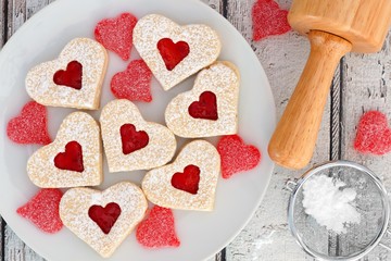 Heart shaped Valentines Day cookies with jam and candies, overhead scene on white wood