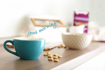 Fototapeta na wymiar Cup of aromatic drink on table. Text GOOD MORNING on background