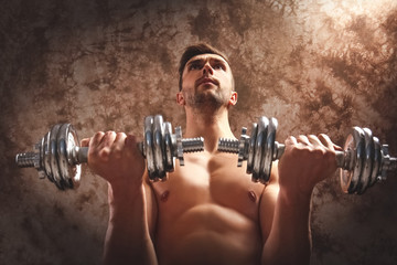 Sporty man doing exercises with dumbbells on grunge background