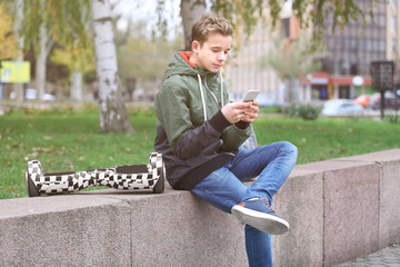 Obraz premium Teenager sitting on parapet with mobile phone and gyroscooter in autumn day