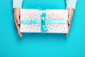 Female hands holding gift box, on color background