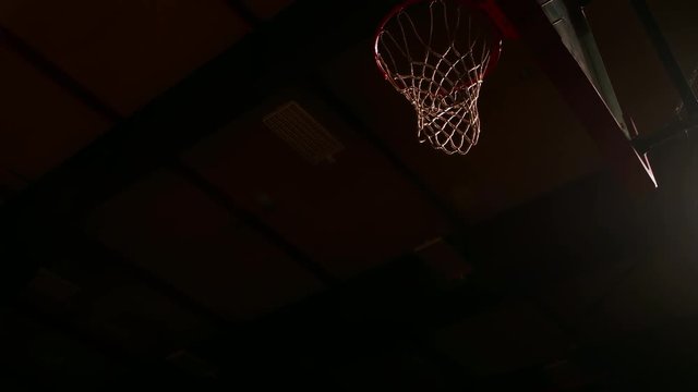 A basketball player dunks the ball, dark lighting, slow motion, view from below