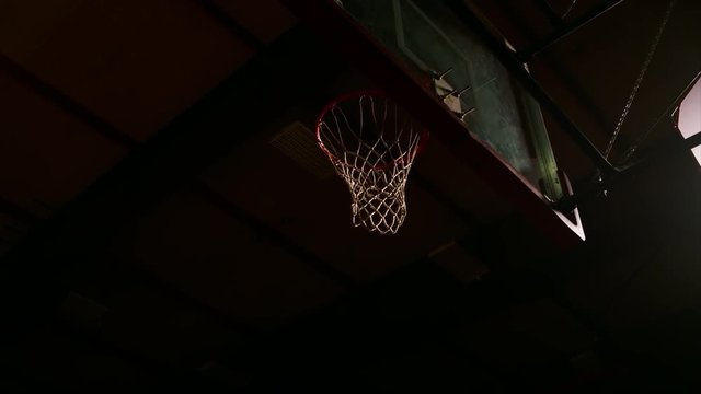 A basketball player dunks the ball once, and then misses, dark lighting, slow motion