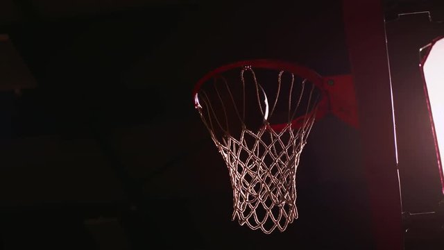 A basketball player dunks the ball, dark lighting, slow motion, view from below