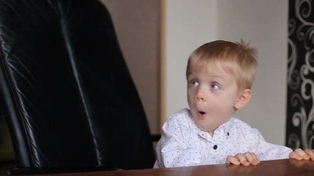Funny baby plays at home. A small businessman kid having fun in a leather armchair.