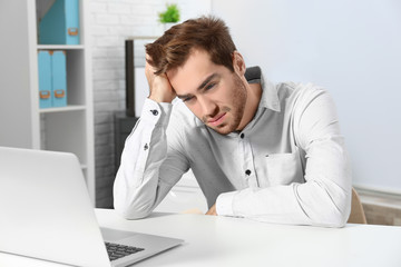 Tired handsome man working with laptop in office