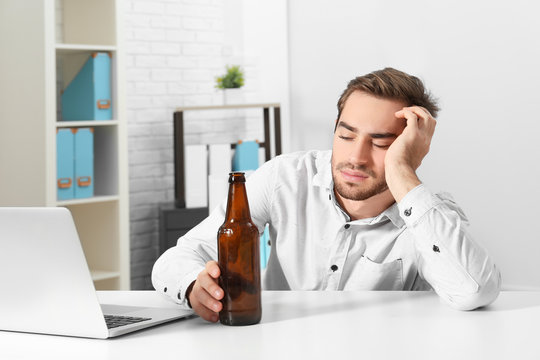 Tired handsome man with bottle of beer in office
