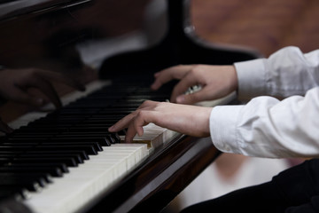 Obraz premium Hands of a child playing the piano closeup in dark colors