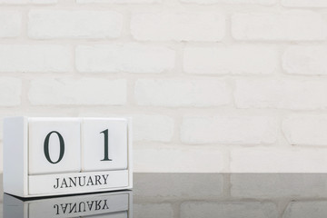 Fototapeta na wymiar Closeup white wooden calendar with black 1 january word on black glass table and white brick wall textured background with copy space , selective focus at the calendar