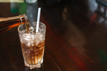 Coca cola splash or sparkling water soft drinks are pouring from bottle into glass with ice on wood...