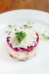 layered salad with herring, beets, carrots, onions, potatoes and eggs close-up on a plate