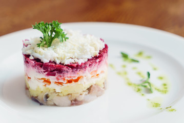 layered salad with herring, beets, carrots, onions, potatoes and eggs close-up on a plate