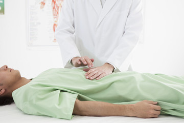 The doctor is examining the stomach of a man