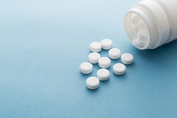 Pills spilling out of pill bottle on blue background. with copy