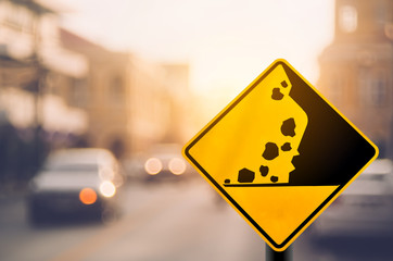 Falling stone warning traffic sign on blur road with colorful bokeh light abstract background.