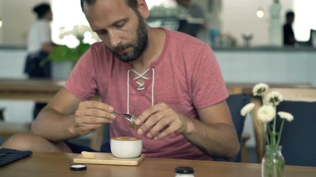 Young man adding sugar into coffee and mixing sitting in cafe, 4k
