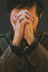 Handcuffed male prisoner in military uniform is praying