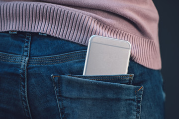 Woman with smartphone in blue jeans back pocket