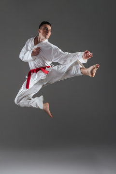 Attractive young sportsman practice in karate isolated over grey background