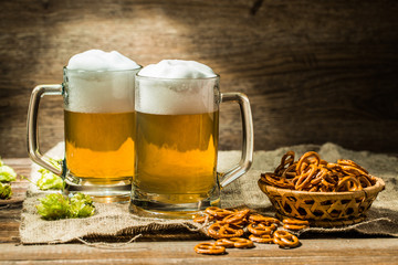 Couple glasses of beer froth with hop and pretzels