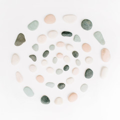 Creative spiral arrangement of colored stones. Mint, pink, beige and grey stones on white. Flat lay, top view