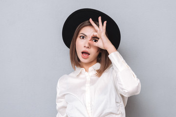 Portrait of a surprised woman in hat looking through fingers