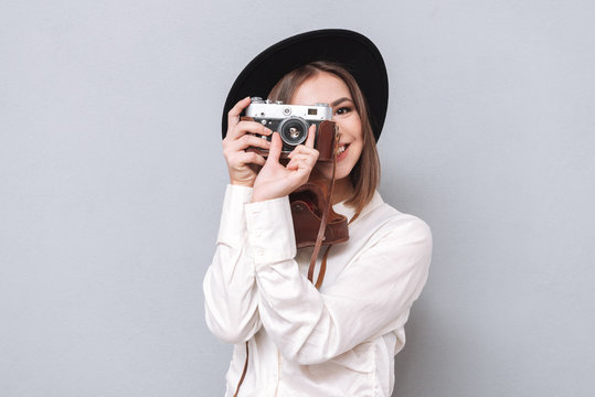 Smiling cheerful girl in hat taking picture with retro camera