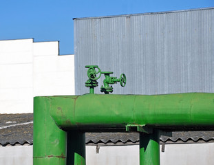 Green painted metal pipe with two valves on the background of the industrial enterprise.