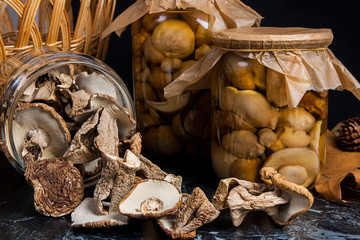 Two glass jars with wild mushrooms on black marble background.