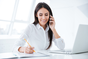 Business woman talking at phone and writing something