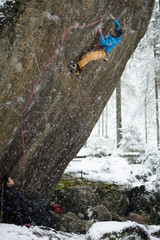 Mountain climber ascending a rock in winter snowy forest. Extrem sports. Karelian nature. 