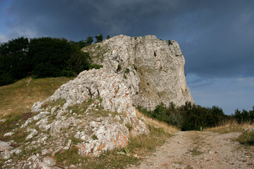 Limestone sunlit cliffs the small path among the grass in Crimean mountains in summer.